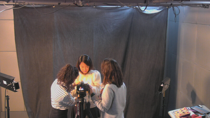 Three people stand around a camera in the Cabot Media Studios setting up for a portrait session. 