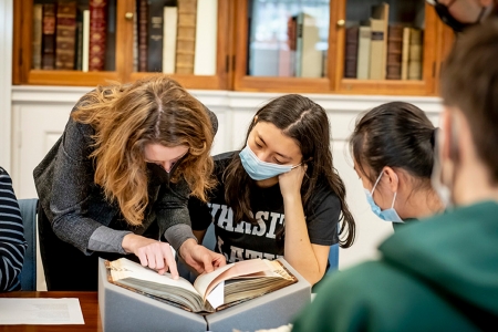 students and professor look at a book