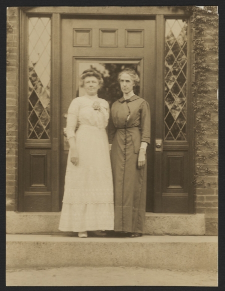 Two women pose for a picture on a step in front of a door.