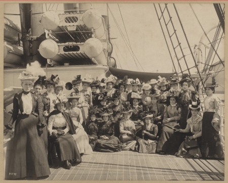 A group of about two dozen women pose for a photo aboard a ship.
