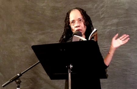 Tracie Morris standing and reading into a microphone at the Poetry Room