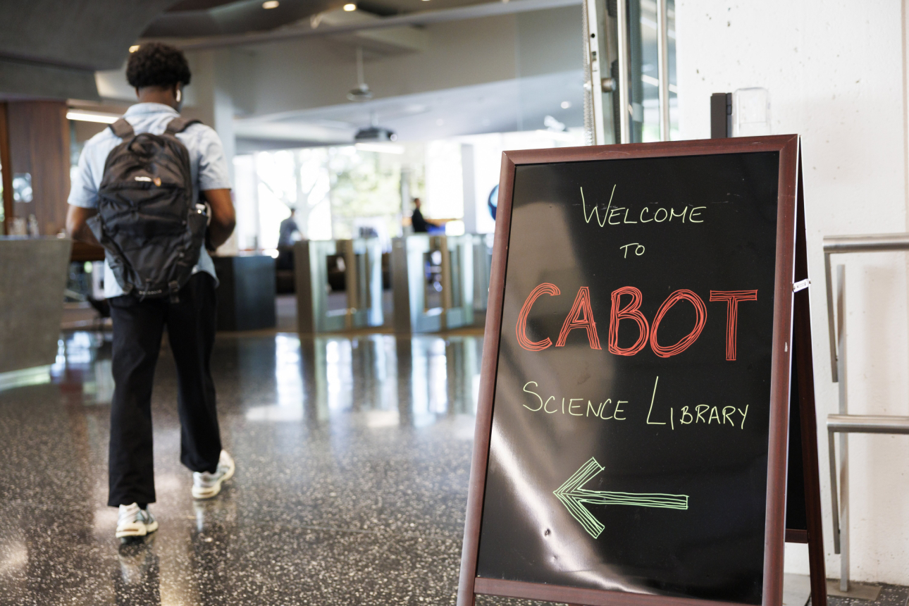 A man with a backpack walks past a sign that ways Welcome to Cabot Science Library