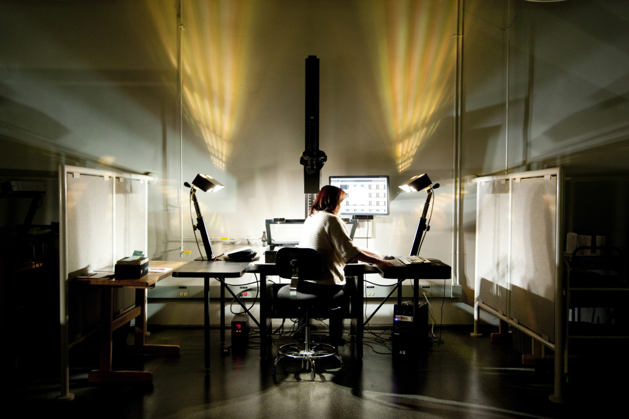 A library staff member sits in a dark studio scanning a rare book 