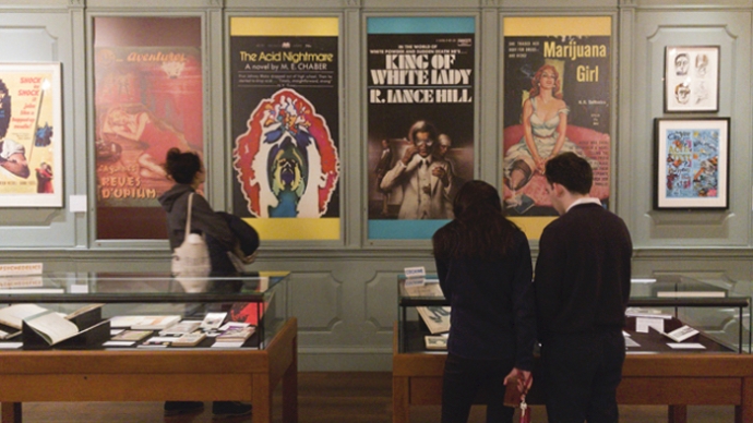 People walk through a gallery and look at displays and prints hung on a wall