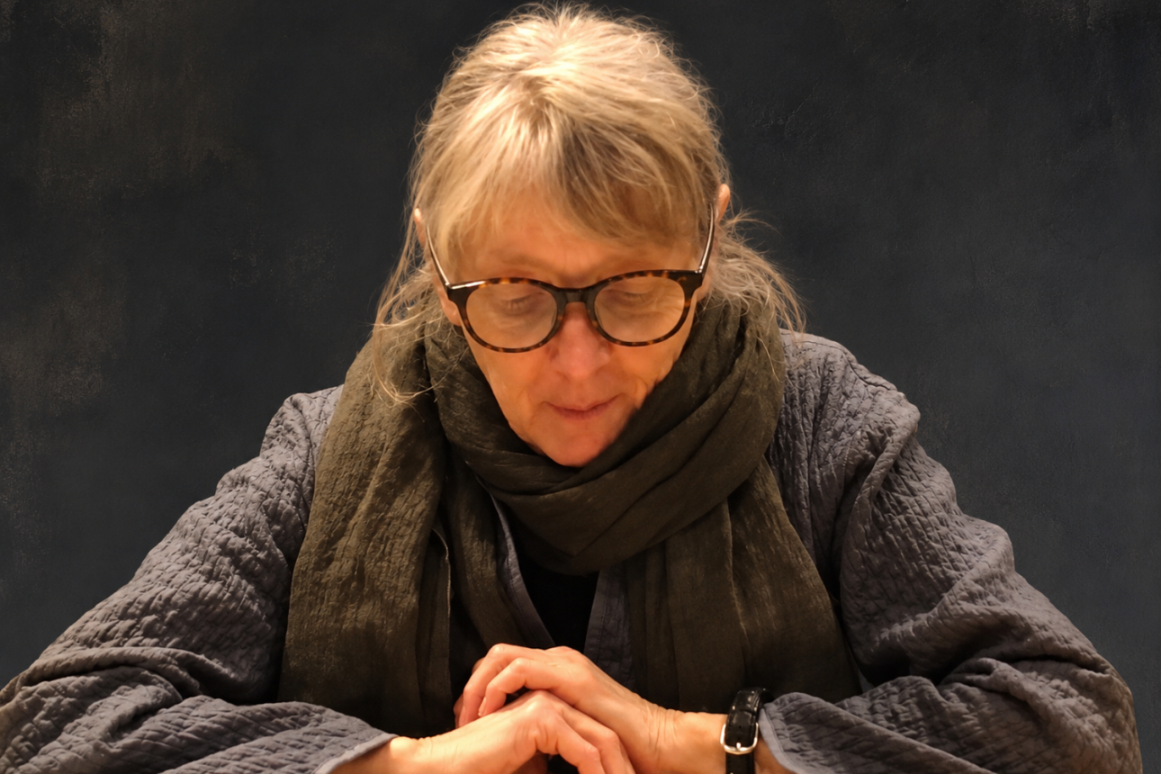 Headshot of Fanny Howe reading from a book with hands folded