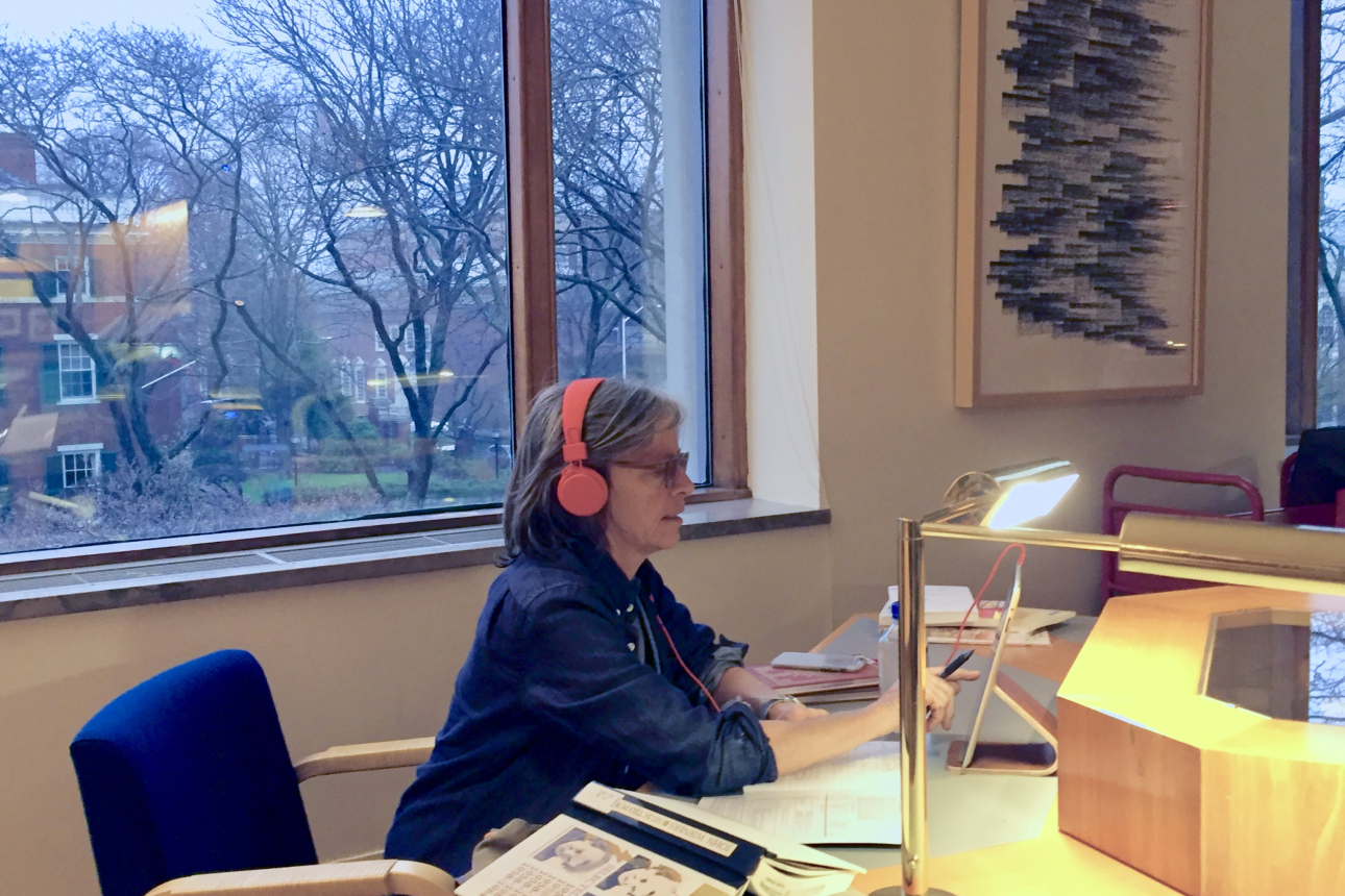 Eileen Myles sits at a computer and wears headphones