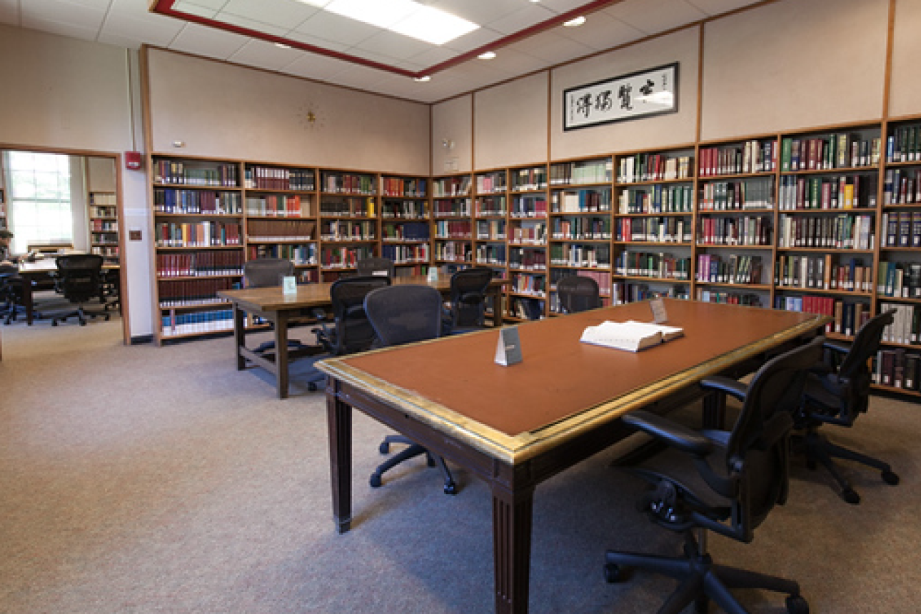 A room mis shown with two large tables with seating, amidst shelves of books