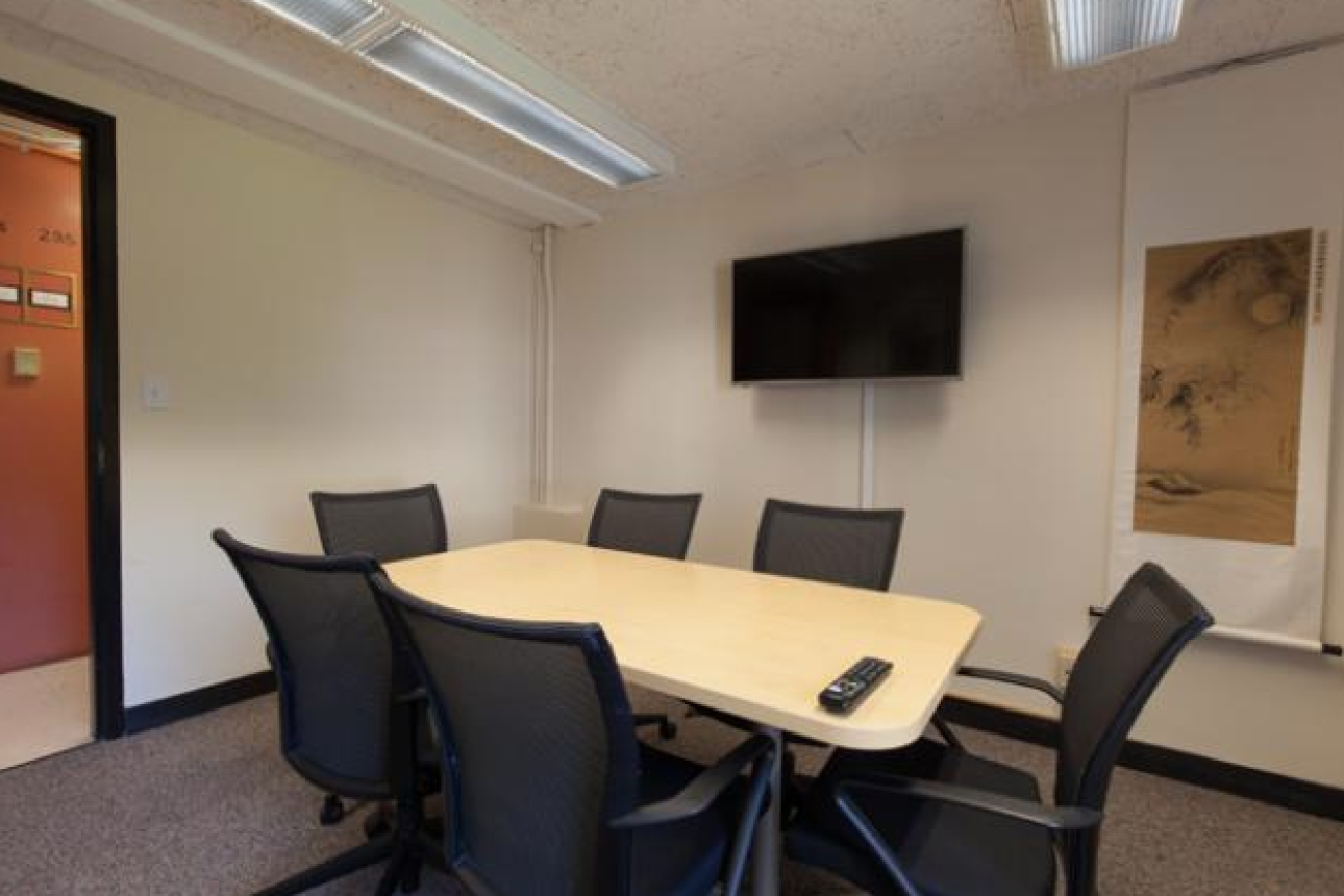 The group study room is show with 6 office chairs around a table, and a tv mounted on the wall