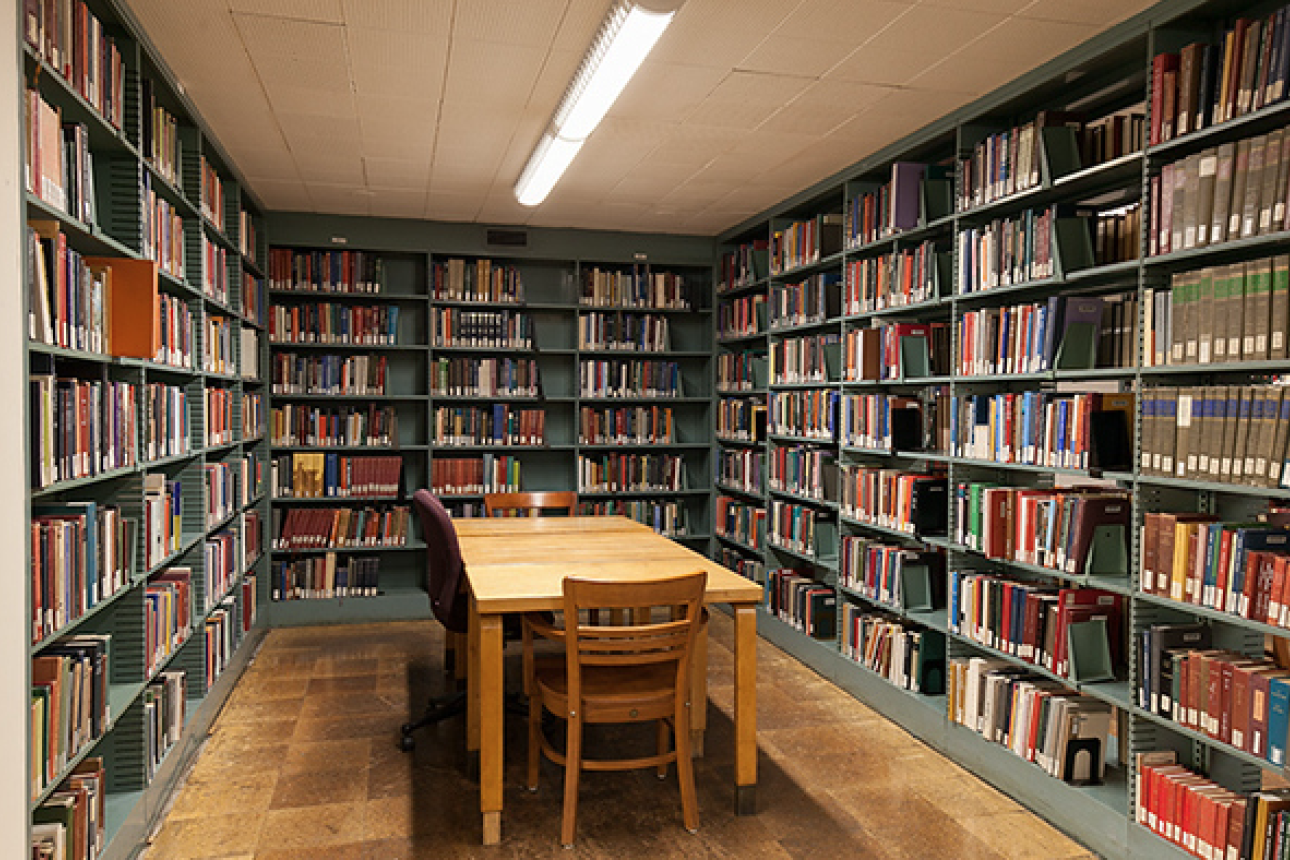 A wooden table with chairs in the middle of shelves of books