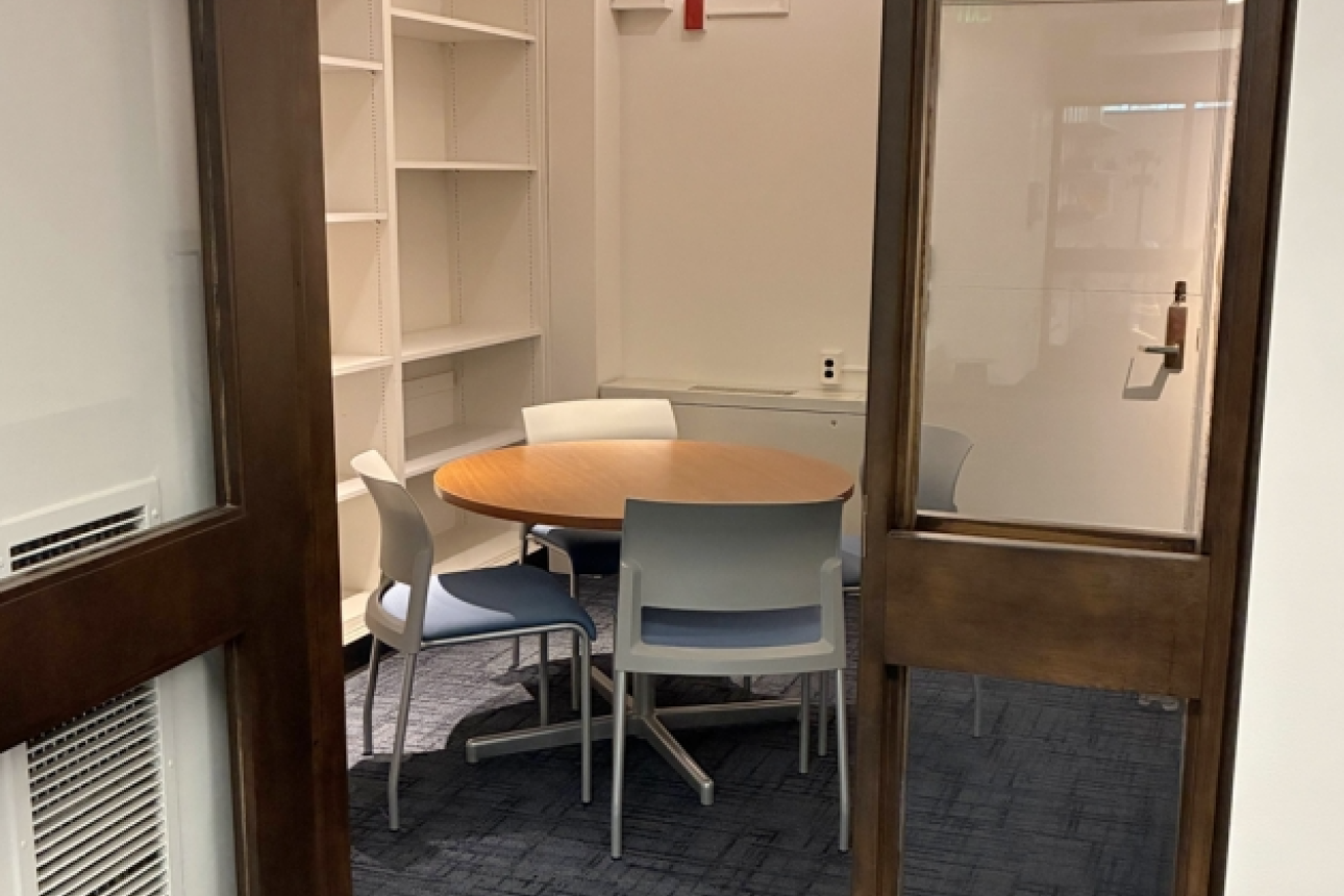 A group study room with a round table, four seats, and shelving