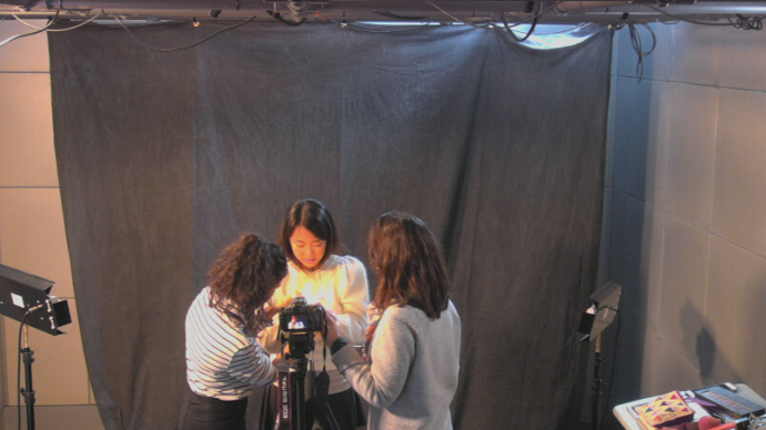 Three people stand around a camera in the Cabot Media Studios setting up for a portrait session.
