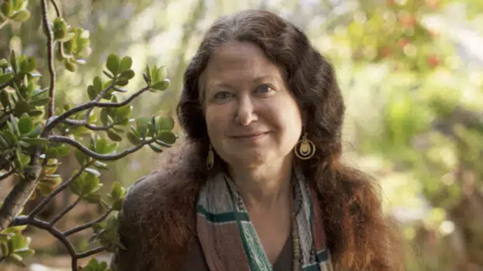 Brown haired woman in the center facing the camera, surrounded by greenery