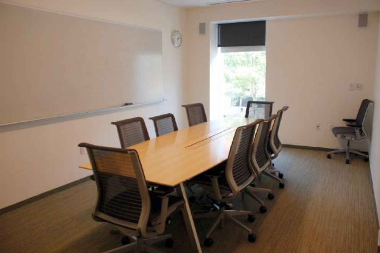 A room with a large conference table, 8 chairs, and a whiteboard