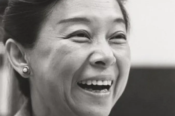 A headshot of a woman wearing a blazer, with her hair pulled up. She is smiling widely.