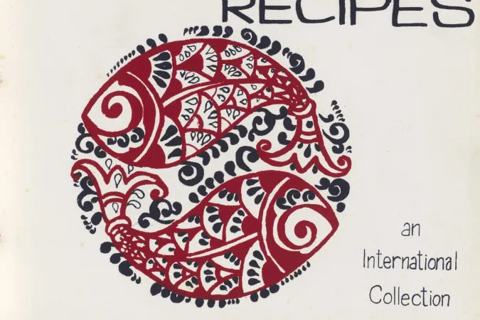 Title page for Recipes, an International Collection. Paper is white and there is a black and red illustration of two decoratively drawn fish forming a large circle in the middle of the page. The text compiled by The United Nations Women's Association, Bangladesh 1980 is along the bottom edge.