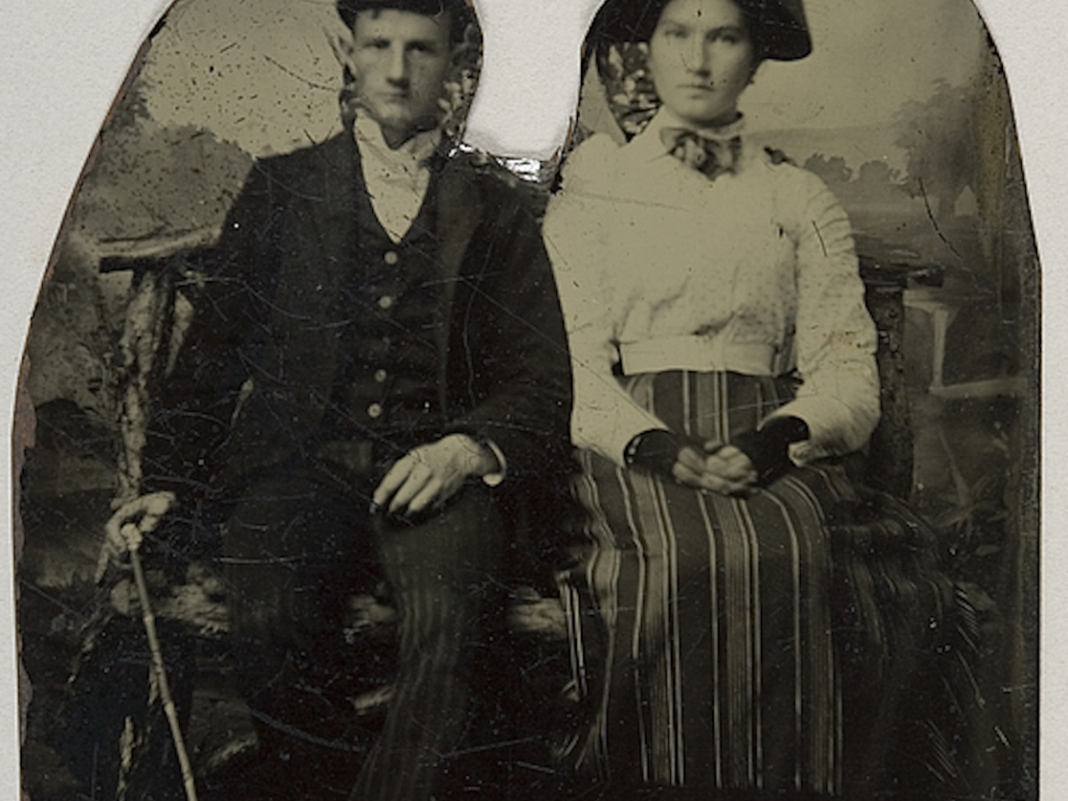 Black and white tintype photo of a couple (white man and woman) sitting side by side, with a space in between cut out leaving jagged outlines