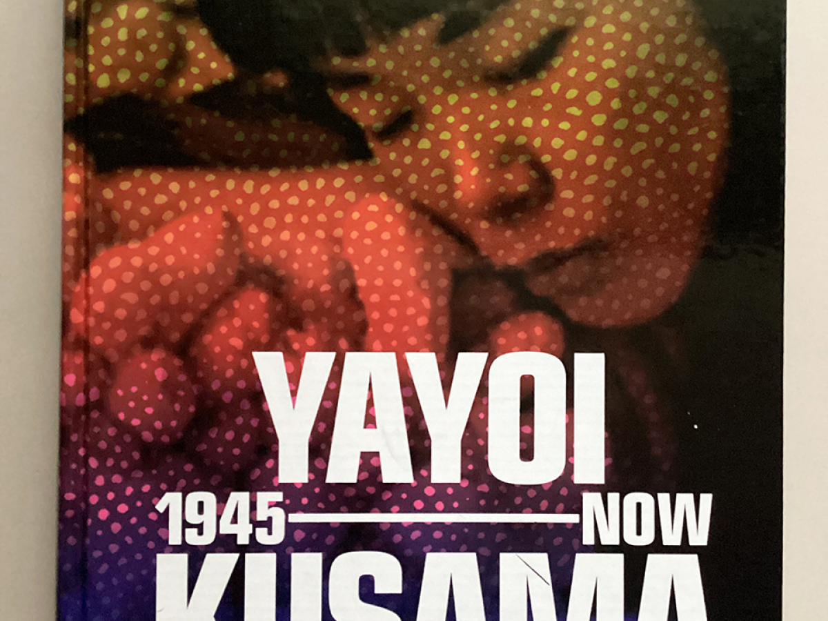 Book cover featuring a photo of Kusama in her twenties, with polka dots on her face, with the title Yayoi Kusama: 1945 – NOW