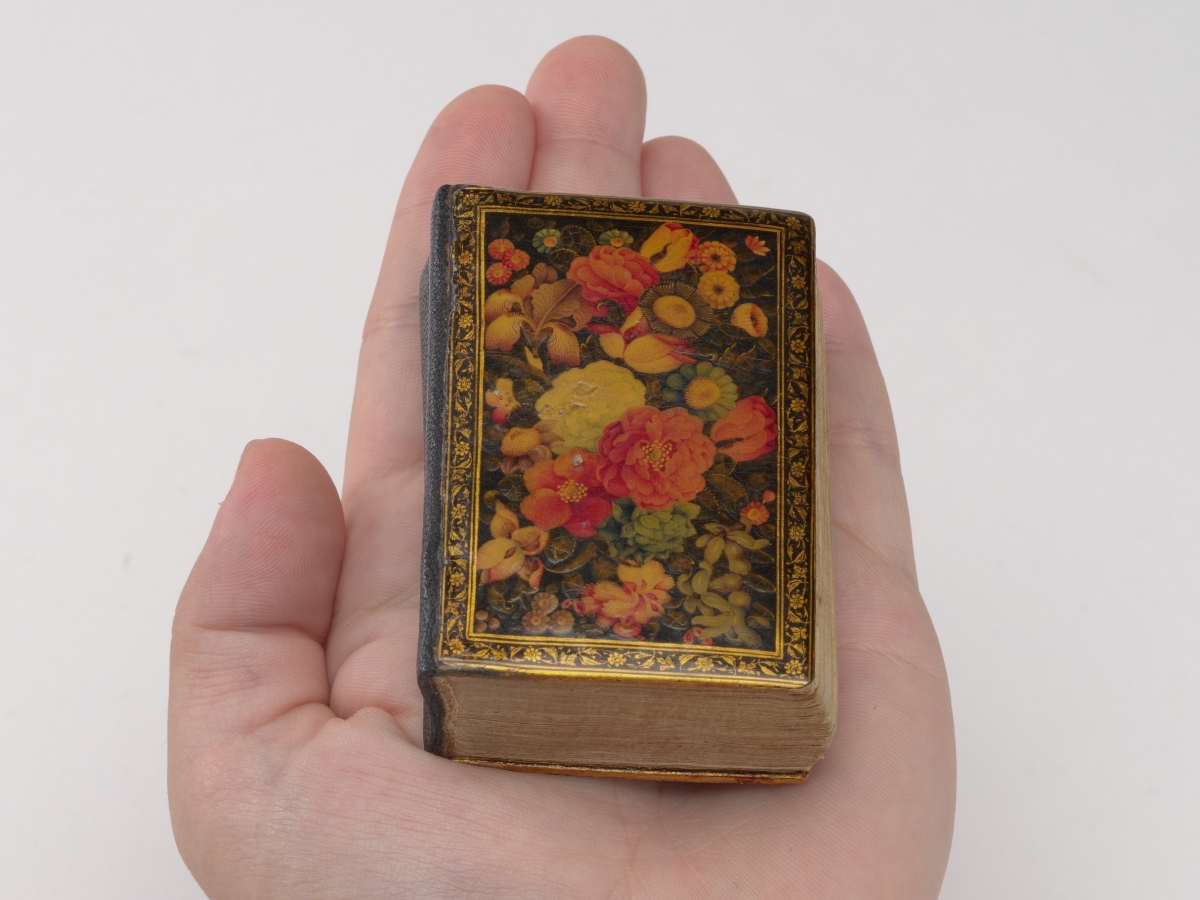 A tiny Qur'an with flowers lacqured on the cover held in the palm of a hand.