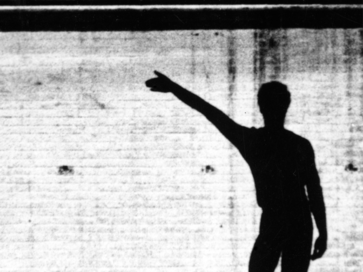 Dancer Merce Cunningham in silhouette, standing with right arm extended and right knee slightly bent.