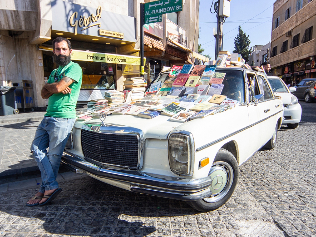 Individual with arms crossed stands next to car with books on it