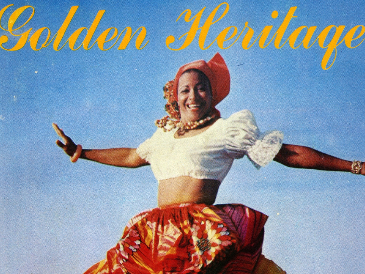 A smiling woman wearing a white top and long red-and-yellow skirt dances on a beach with ocean and sky in the background.
