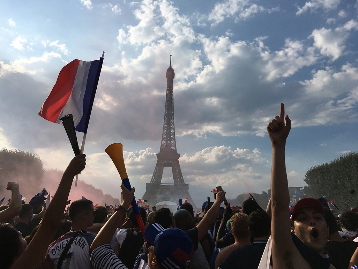 a crowd holding up their hands and a flag of France in front of the Eiffel Tower
