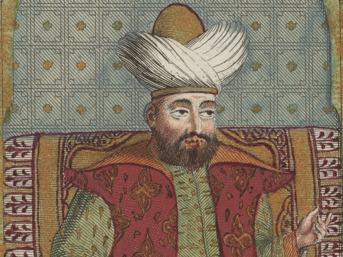 Middle eastern man wearing headdress, green robe, and red cloak.