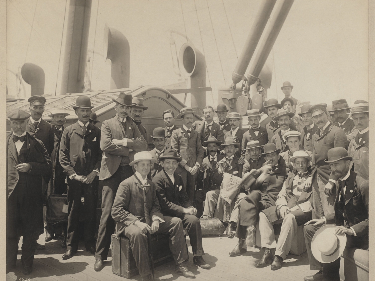 Men in formal clothes and hats on the deck of a U.S. naval ship.