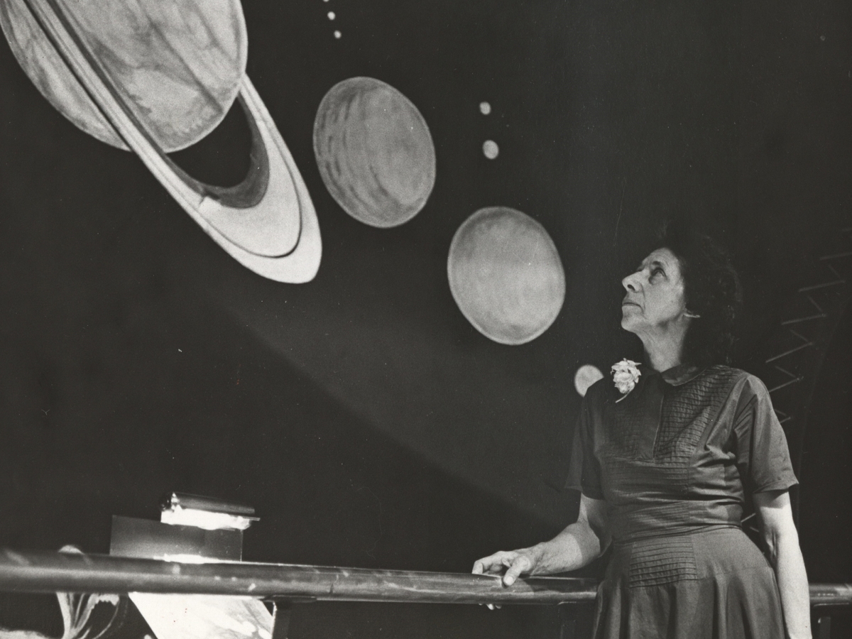 A Woman stands in front of an astronomy exhibition, looking up at a model of Saturn and other planets.