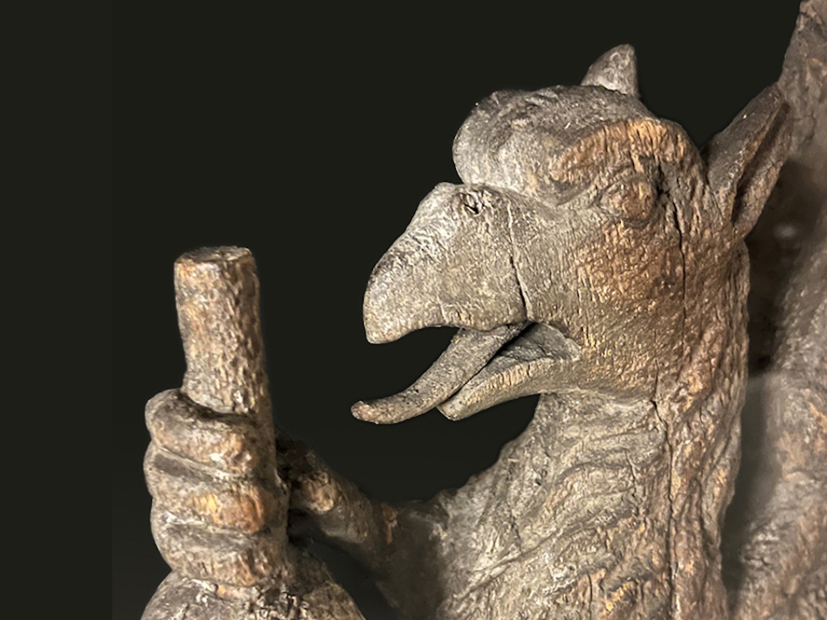 Wood carving of a griffin with its mouth open and claws clutching the stem of an ink ball.