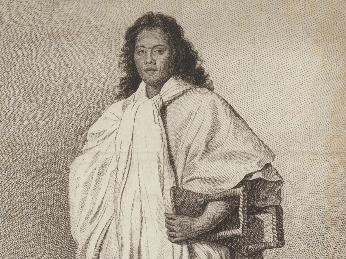 Man with long, wavy black hair and white robe carrying footstool under his arm. 