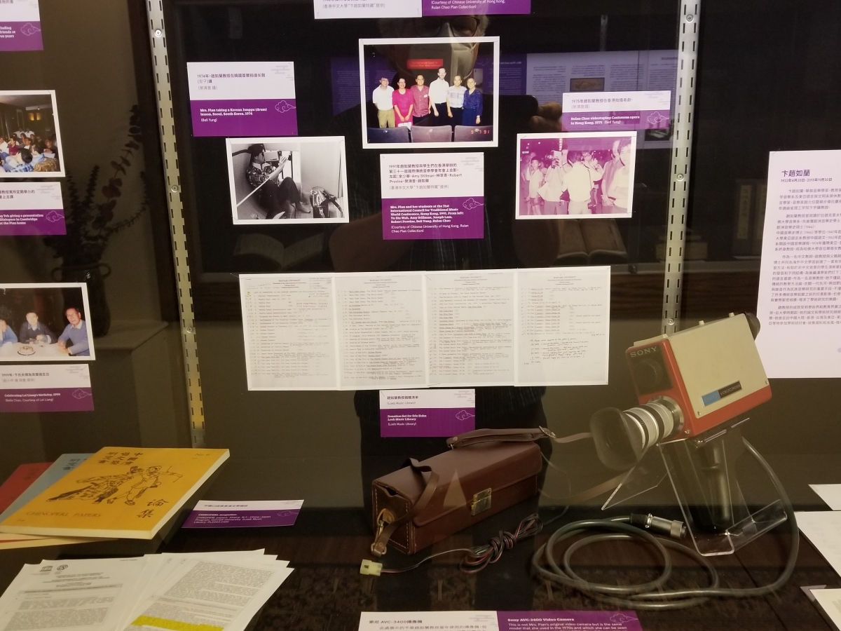 An exhibit case filled with color photographs, magazines and letters, and a bulky handheld video camera.
