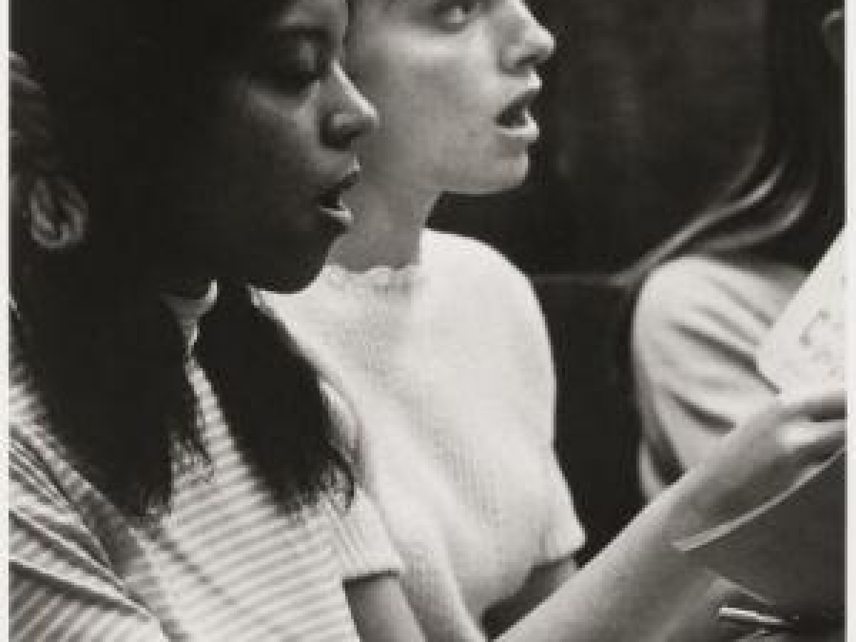 Two people in casual clothes, holding music and singing during a choir rehearsal.
