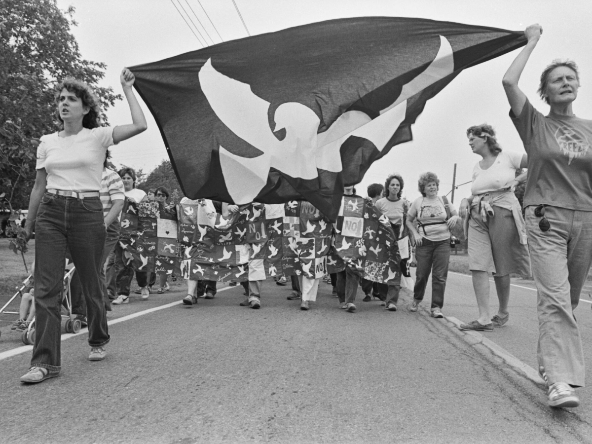 A group of women are marching on a street with a banner held above their heads.