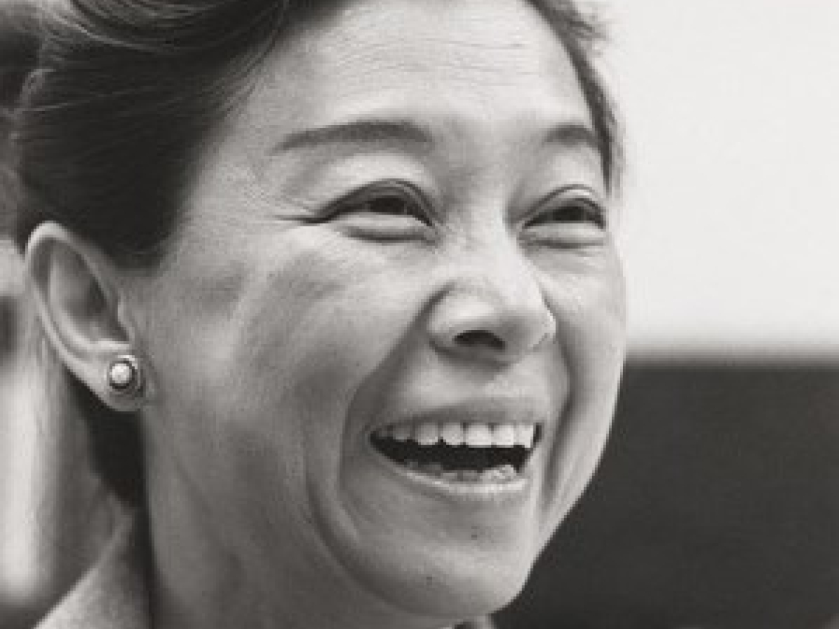 A headshot of a woman wearing a blazer, with her hair pulled up. She is smiling widely.