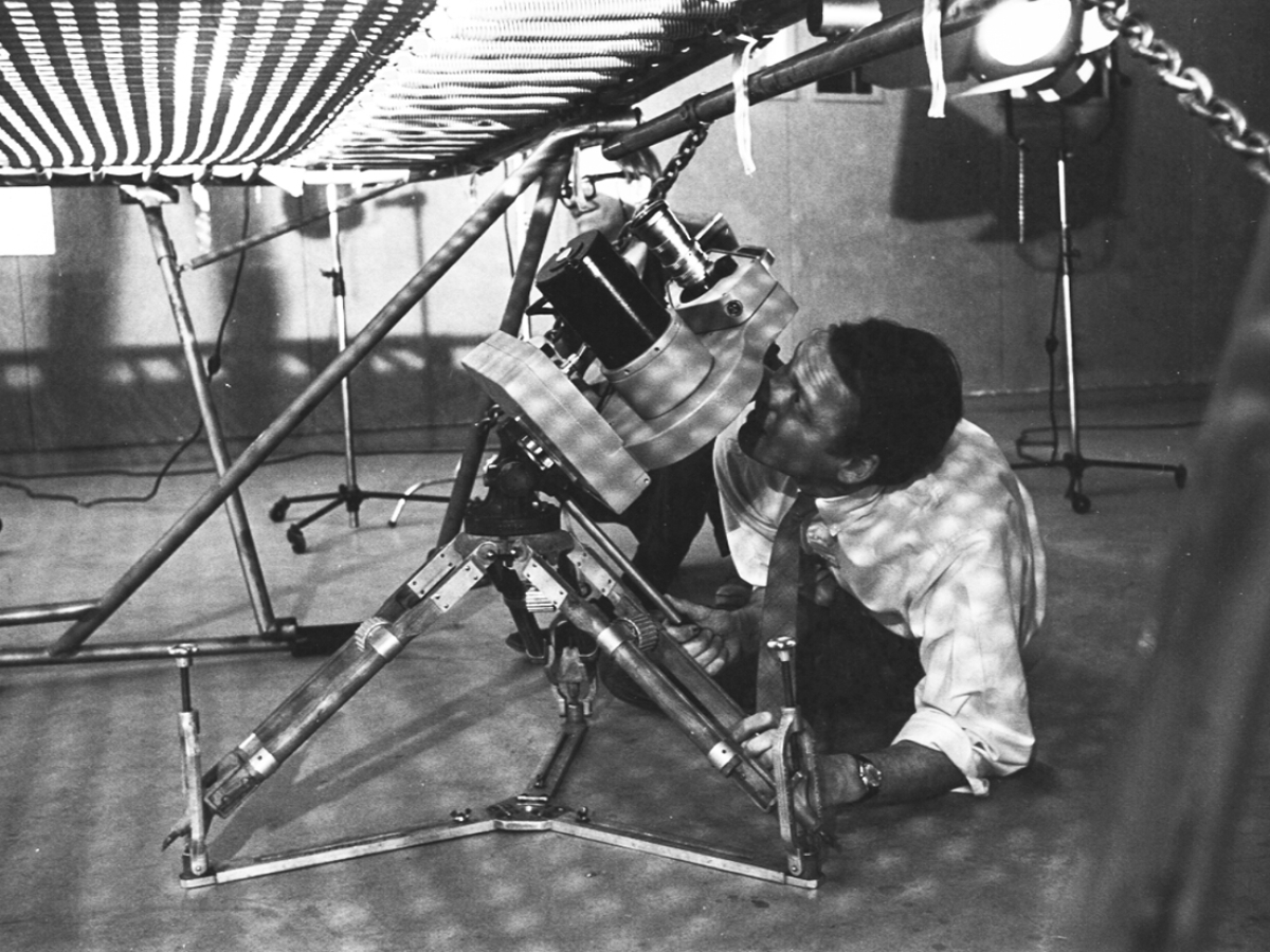 a black and white image of a man filming a low angle shot with a 16mm camera through mesh