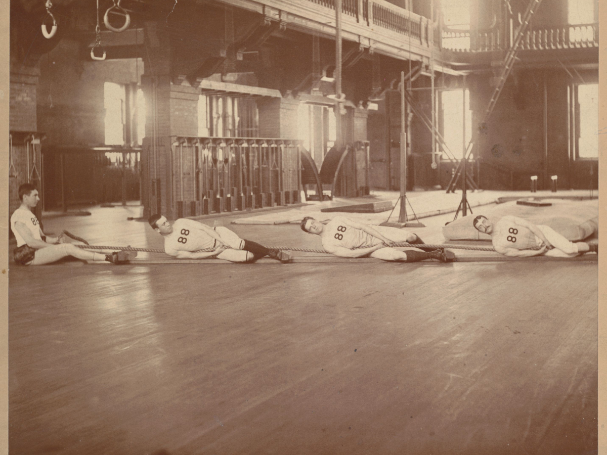 Black and white photo of male students on a gymnasium floor pulling on a rope