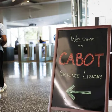 A man with a backpack walks past a sign that ways Welcome to Cabot Science Library