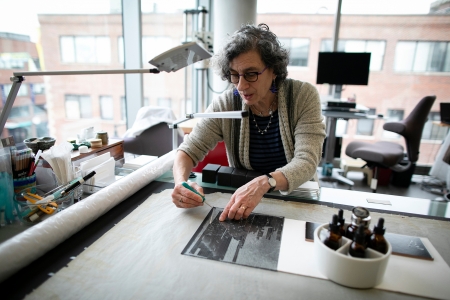 Conservator leans over print on large table with eyedropper