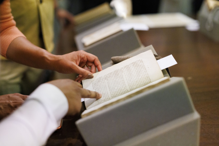 Closeup of a hand pointing to a book open on a stand.