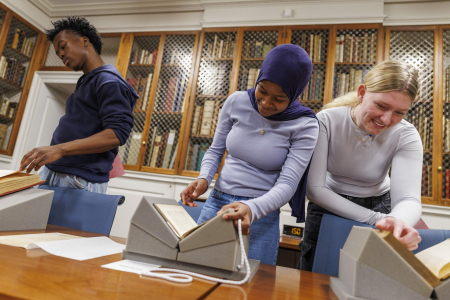 3 students flip through various rare books as part of a class at Houghton Library