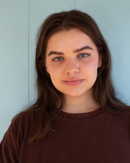 Elizabeth Propst, wearing a dark top and with dark brown hair, looks at the camera