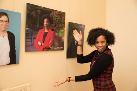 Woman gesturing to a portrait of herself on the wall behind her.