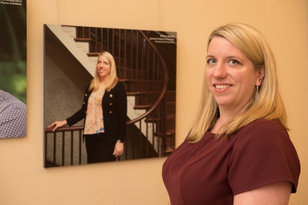 A woman poses in front of a photo of herself hanging on the wall behind her.