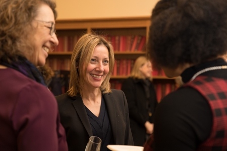 Three women smile as they talk together at a reception.
