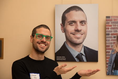 A man gestures to the photo portrait of himself behind him.