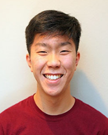 Elijah Suh, wearing a red top, smiles and looks at the camera