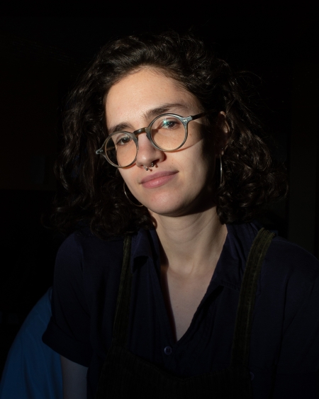 Mika Simoncelli, wearing glasses and with curly brown hair, smiles and looks away from the camera