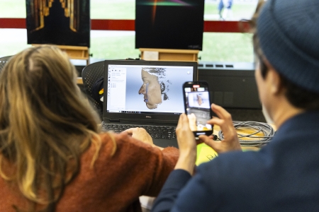 A woman sits working at a laptop, and on the laptop screen we can see a face in 3D starting to form.