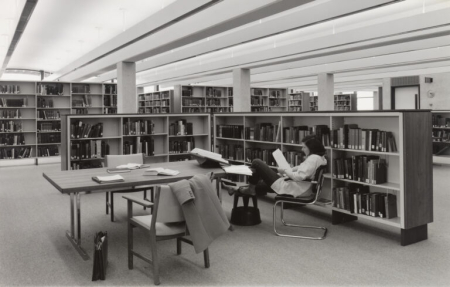 A woman sits at a desk reading a book in this black and white photo